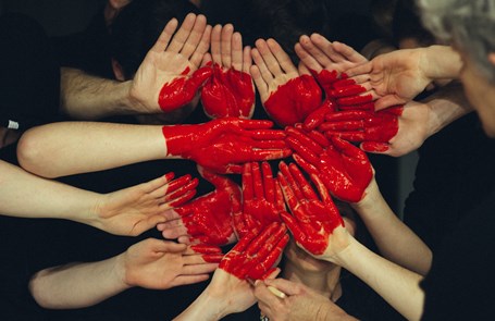 Lots of hands held together and painted red to form a heart shape