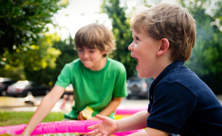 Two boys playing with a paddling pool and laughing with delight