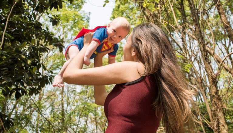 A mum swinging a baby wearing a superman outfit
